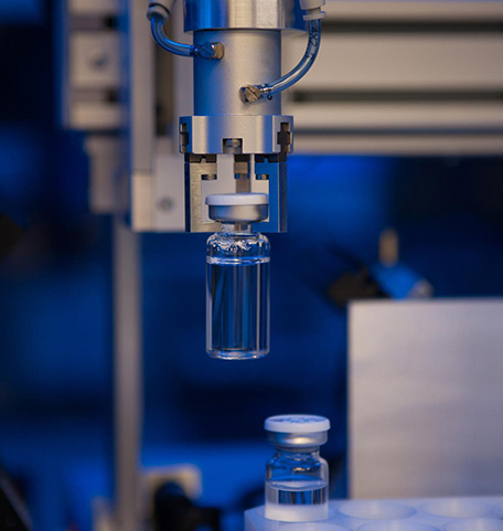 Ein Roboterarm in der Produktion fasst ein Glasfläschchen für Arzneimitte
